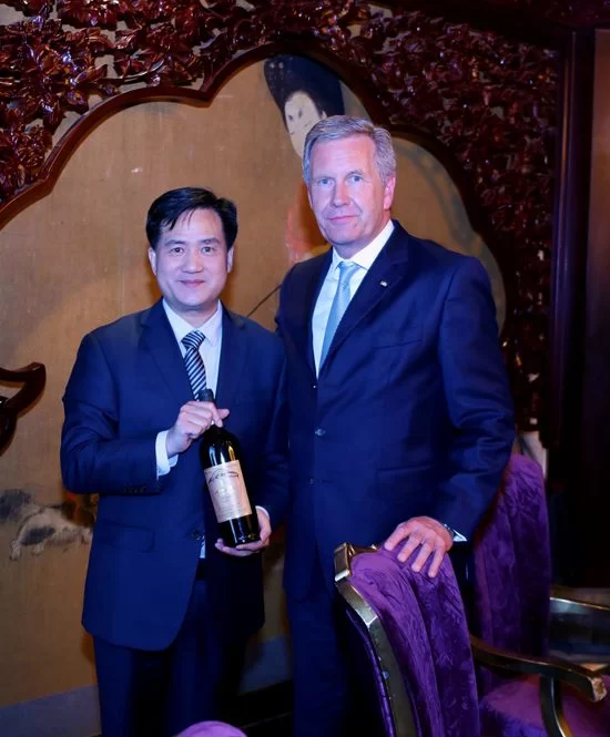 德国前总统武尔夫是如何喝上神沟九寨红的?(图3) 全球中小企业联盟主席、德国前总统武尔夫和全球中小企业联盟秘书长曹方与“神沟九寨红”合影